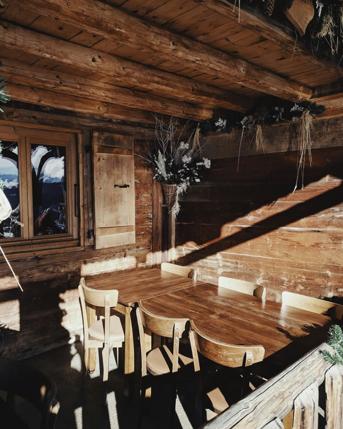 Terrasse couverte d'un chalet en bois, tables et chaises au soleil